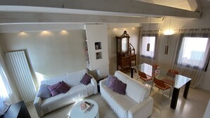 A living room with a white sofa, a round coffee table, a dining table with chairs, a wooden cabinet, and a large window with curtains. - Apartment, A stone's throw from St. Mark's with a lovely view  (Venezia)