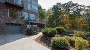 Une maison moderne à deux étages, dotée d’un garage, d’un porche abrité et d’un jardin aménagé avec différents arbustes et arbres.