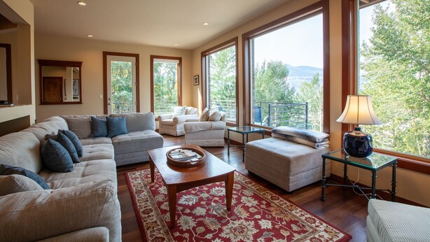 Un salon spacieux comprenant un grand canapé d’angle, une petite banquette, une table basse et une petite table d’appoint. De grandes fenêtres offrent une vue sur la verdure et les collines.