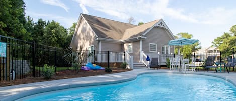 A swimming pool with a house in the background, surrounded by a fence and trees.