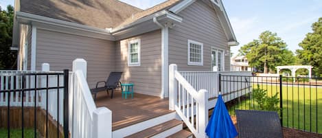Uma casa com um deck de madeira, guarda-corpos brancos e um guarda-sol azul.