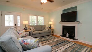 A living room with a sofa, two lamps, a fireplace, and a TV. - Single level, Interior home with Private Pool and Golf Cart in Spinnaker's Reach (Emerald Isle)