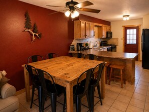 A kitchen with wooden cabinets, a dining table with chairs, a ceiling fan, and a red wall.