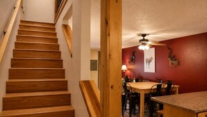 A wooden staircase leading to a dining area with a table and chairs, a ceiling fan, and a red wall with a deer head decoration. - Mountain Memories, Walk to Ski Area, Town, Fishing (Red River)