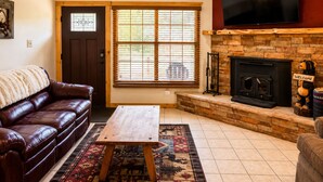 A living room with a leather sofa, a wooden coffee table, a fireplace, and a TV mounted on the wall. - Mountain Memories, Walk to Ski Area, Town, Fishing (Red River)