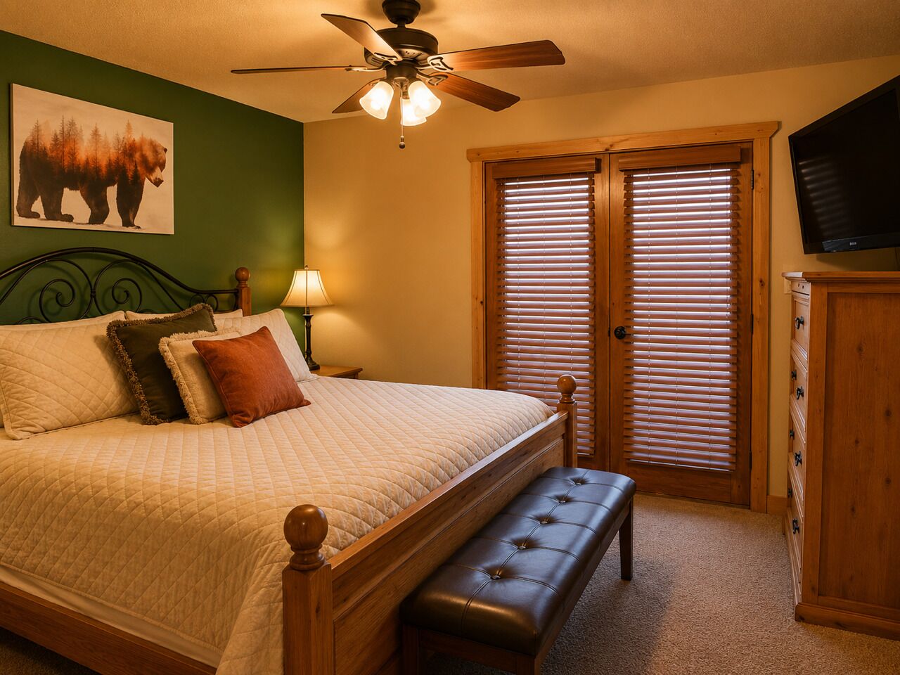 A bedroom with a bed, a bench, a ceiling fan, a TV, and a window with blinds.