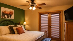 A bedroom with a bed, a bench, a ceiling fan, a TV, and a window with blinds. - Mountain Memories, Walk to Ski Area, Town, Fishing (Red River)