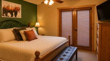 A bedroom with a bed, a bench, a ceiling fan, a TV, and a window with blinds.