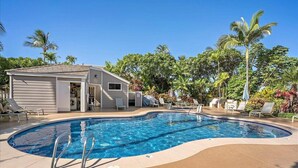Une piscine avec des chaises longues et un petit bâtiment, le tout entouré de palmiers.