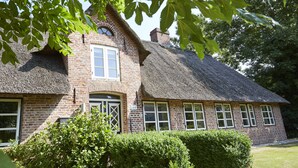 A traditional brick house with a thatched roof and multiple windows.