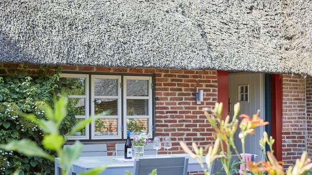 A brick building with a thatched roof, a window, and a table with a bottle and glasses.