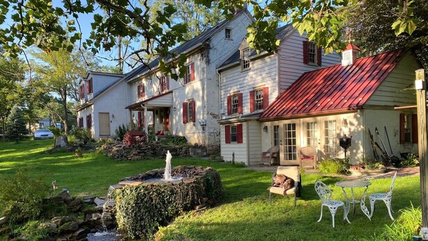 Una casa tradicional con una fuente de piedra, un pequeño estanque y un jardín bien cuidado con mobiliario de exterior.