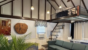 Una sala de estar tipo loft con techo alto, vigas a la vista, una litera y una escalera.