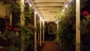 Un sendero cubierto en un jardín, con columnas blancas y luces de cuerda.