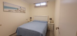 Ein Schlafzimmer mit Bett, Nachttischen, einer Lampe, einem Gemälde und einem Fenster mit Vorhängen.