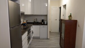 A compact kitchen with white cabinets, stainless steel appliances, and a wooden cabinet with a vase.