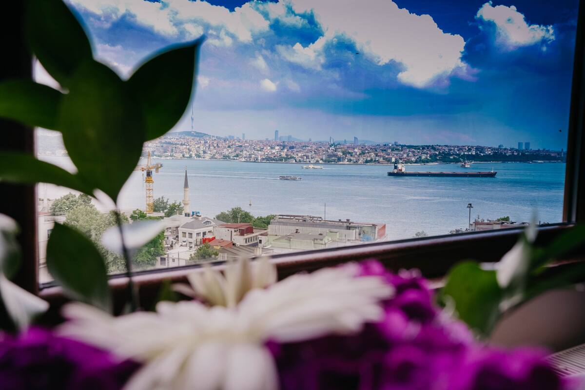 A view through a window with a cityscape, including a large ship on the water and a crane in the foreground.