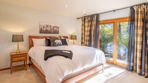 A bedroom with a large bed, two bedside tables with lamps, a painting on the wall, and a view through the window. - Game Room, Sauna, Bonus Apartment Near Wintergreen Resort! (Nellysford)