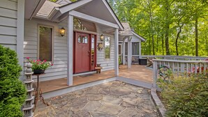 A house with a stone porch, a red door, and a small garden with a statue and flowers. - Game Room, Sauna, Bonus Apartment Near Wintergreen Resort! (Nellysford)