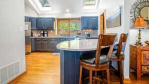 A kitchen with dark blue cabinets, a central island with chairs, skylights, and a view of greenery outside. - Game Room, Sauna, Bonus Apartment Near Wintergreen Resort! (Nellysford)