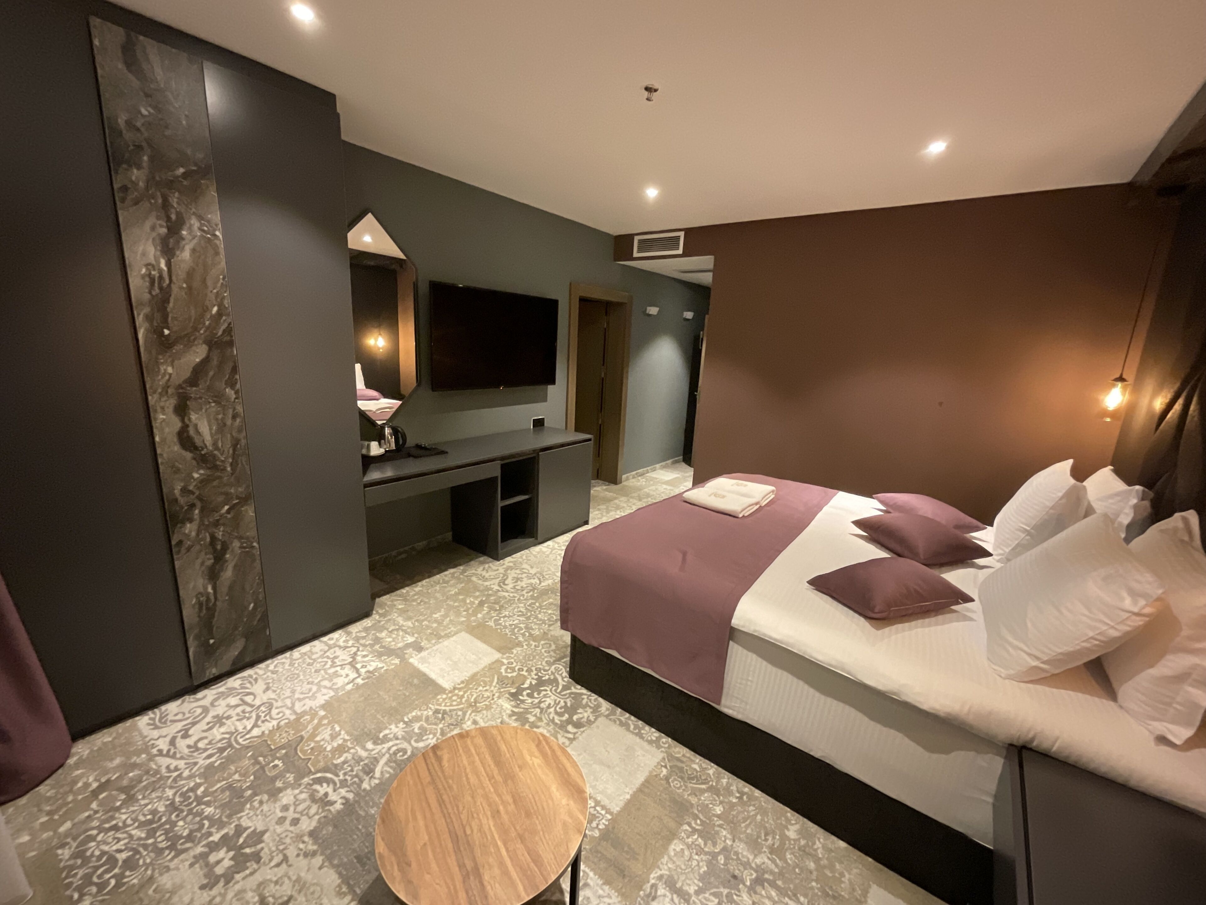 A modern hotel room with a large bed, a TV, a desk, and a round table.