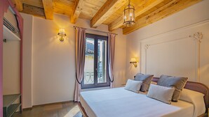 Een slaapkamer met een houten plafond, een groot bed met veel kussens, twee wandlampen en een raam met gordijnen.
