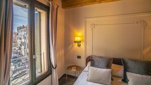 Een hotelkamer met een bed, kussens, een nachtkastje, een lamp en een raam met gordijnen.