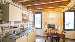 Een keuken met een inbouwoven, een eethoek met tafel en stoelen, en een stenen muur met een televisie.