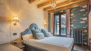 Ein Schlafzimmer mit Holzbalkendecke, einem Bett mit vielen Kissen, zwei Nachttischlampen und einem Fenster mit Vorhängen.