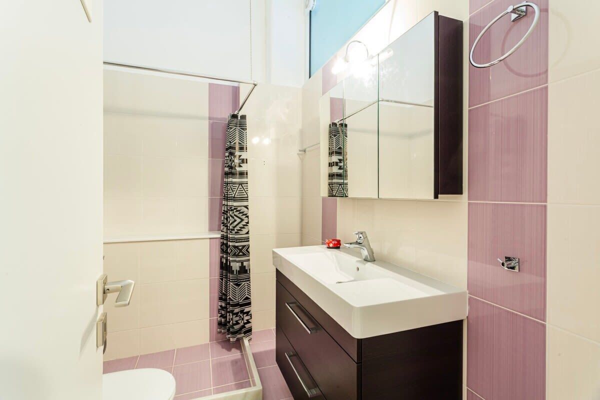 A bathroom with a white sink, a mirror, a towel ring, and a patterned shower curtain.