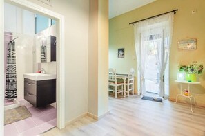 A bathroom with a sink, mirror, and patterned shower curtain. There is a dining area with a table and chairs, and a window with curtains.