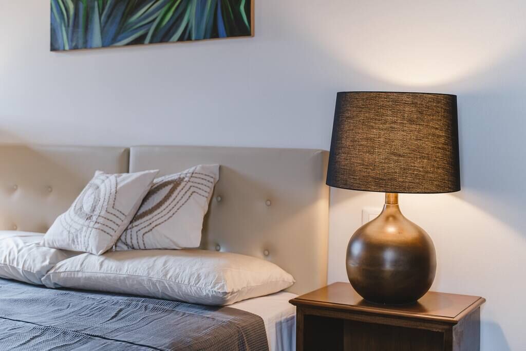 Un lit bien fait, doté d’une tête de lit capitonnée, d’une lampe de chevet et d’un tableau accroché au mur.