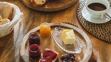 A breakfast setting with a variety of food items including a bagel, butter, jams, and coffee on a wooden table.