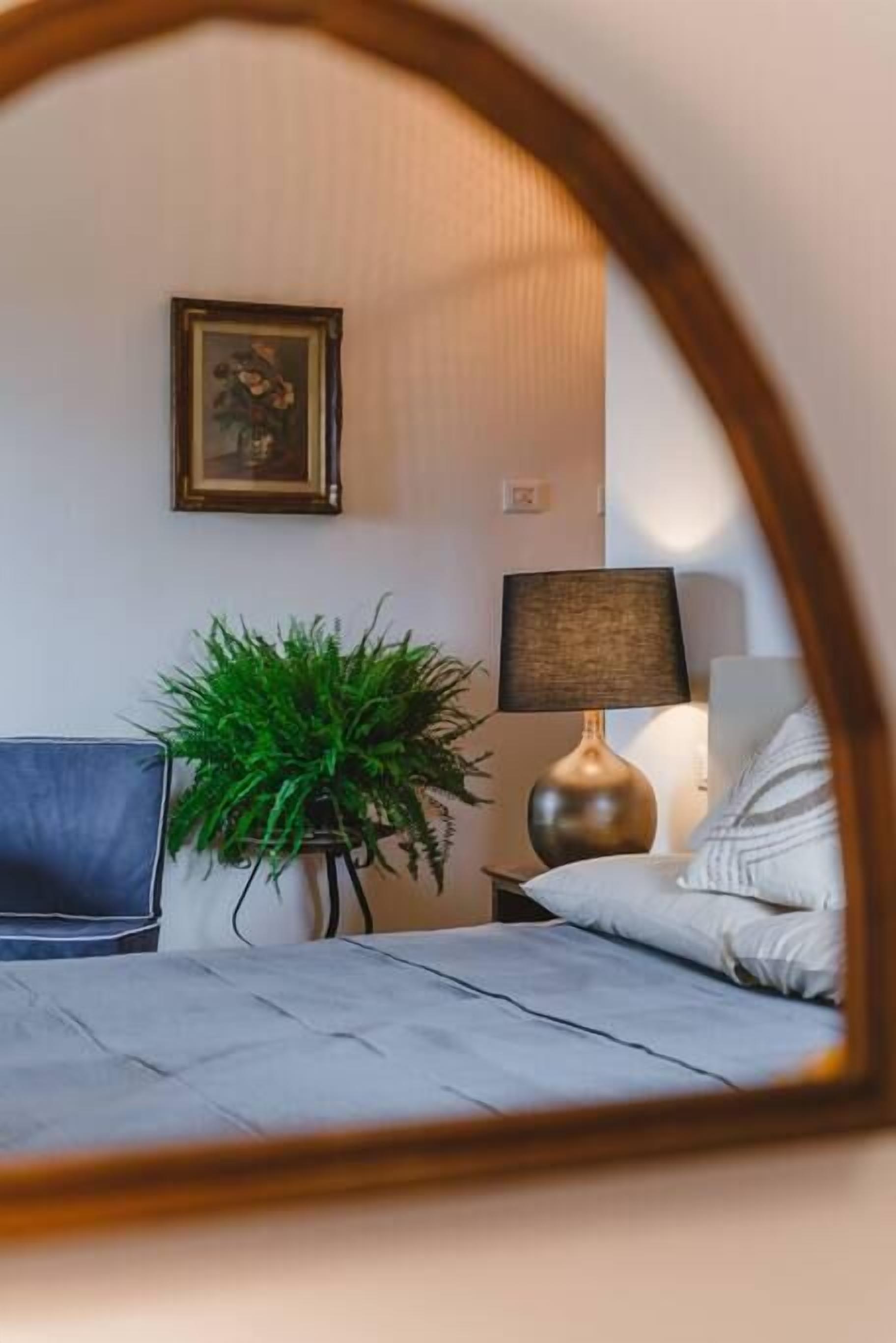 A bedroom with a bed, a desk, a lamp, a plant, and a framed picture on the wall.
