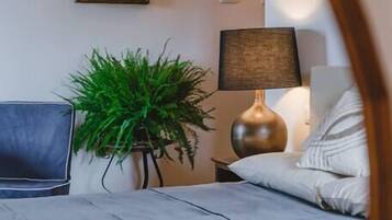 A bedroom with a bed, a desk, a lamp, a plant, and a framed picture on the wall.