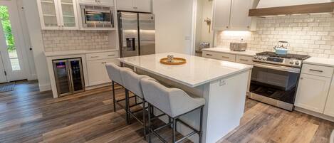 A modern kitchen with white cabinetry, stainless steel appliances, a central island with bar stools, and a wooden floor.