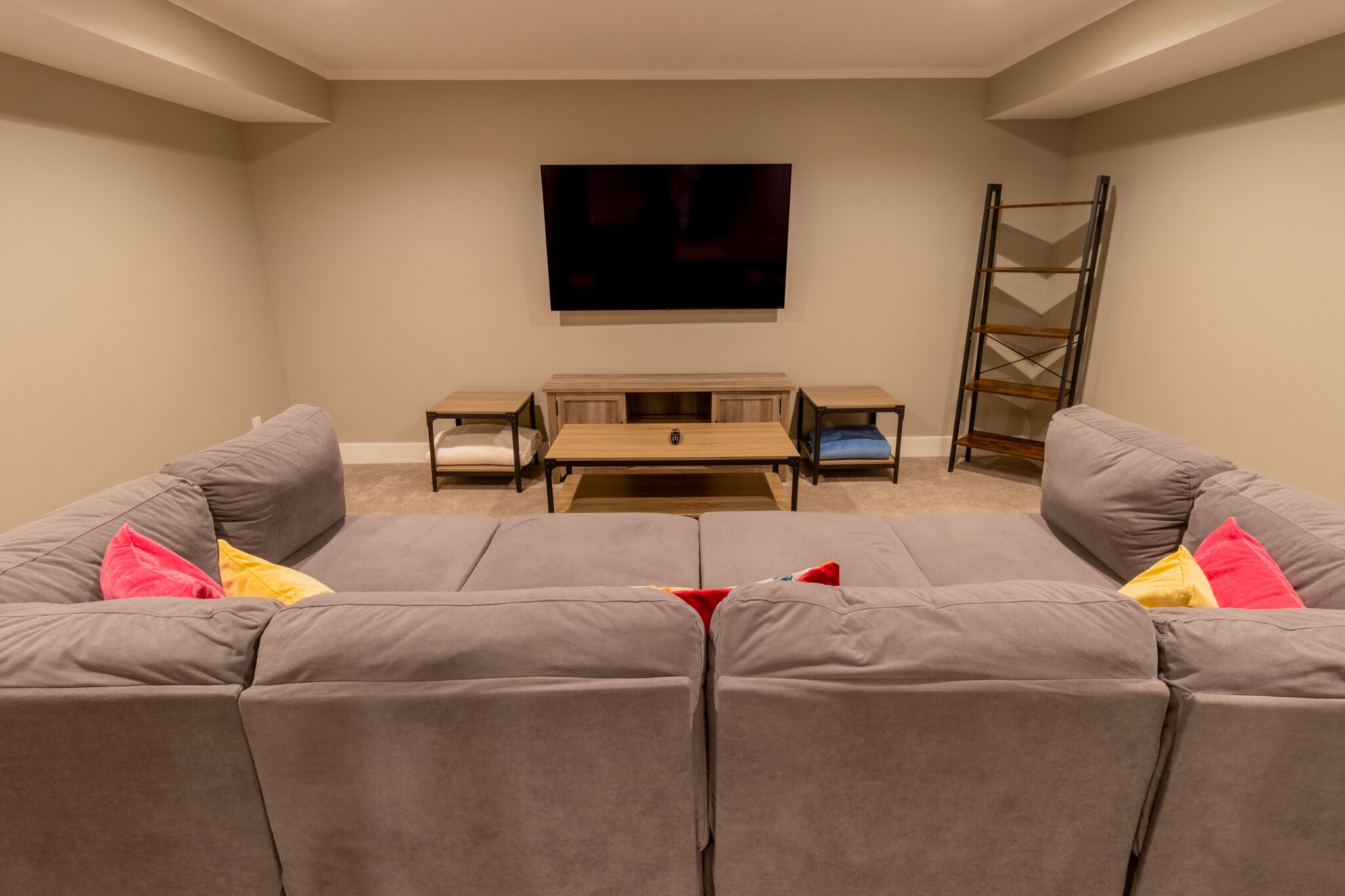 A living room with a large grey sectional sofa, a wooden coffee table, and a TV mounted on the wall.