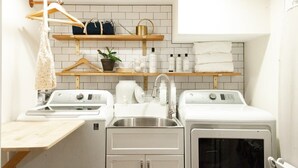 Um espaço de lavanderia compacto, com duas máquinas de lavar, uma pia e prateleiras com produtos de higiene e toalhas.