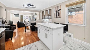 Een moderne keuken met een marmeren aanrechtblad, witte keukenkastjes en een eethoek met een zwarte leren bank.