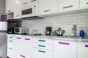 Een moderne keuken met witte kasten, een magnetron, een koffiezetapparaat en een waterkoker.