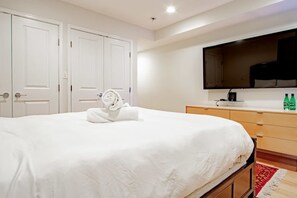 A hotel room with a large bed, a flat-screen TV mounted on the wall, a wooden dresser, and a red and white patterned rug. - Modern 2BR Apartment Near Union Station DC (Washington)