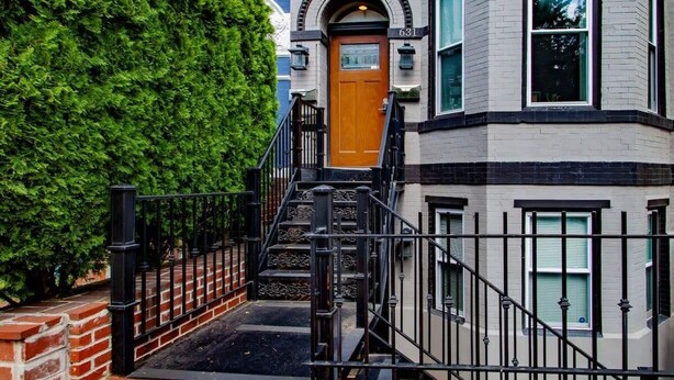 Ein Eckgebäude mit einer Holztür, einem Ziegelunterbau und einer schwarzen Metalltreppe, die zum Eingang führt.