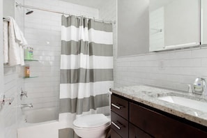 A modern bathroom with a bathtub, toilet, and vanity with a sink. - Modern 2BR Apartment Near Union Station DC (Washington)