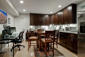 A modern kitchen with dark wooden cabinets, a stainless steel refrigerator, and a dining area with a table and chairs. - Modern 2BR Apartment Near Union Station DC (Washington)