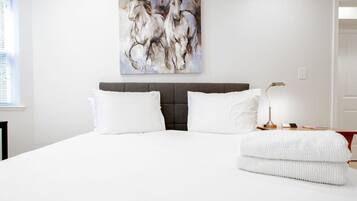 A bedroom with a large bed, white bedding, a grey headboard, and a wall-mounted painting of horses.