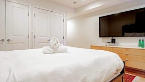 Ein Hotelzimmer mit einem großen Bett, einem an der Wand montierten Flachbildfernseher, einer Holzkommode und einem Teppich mit rotem und weißem Muster.