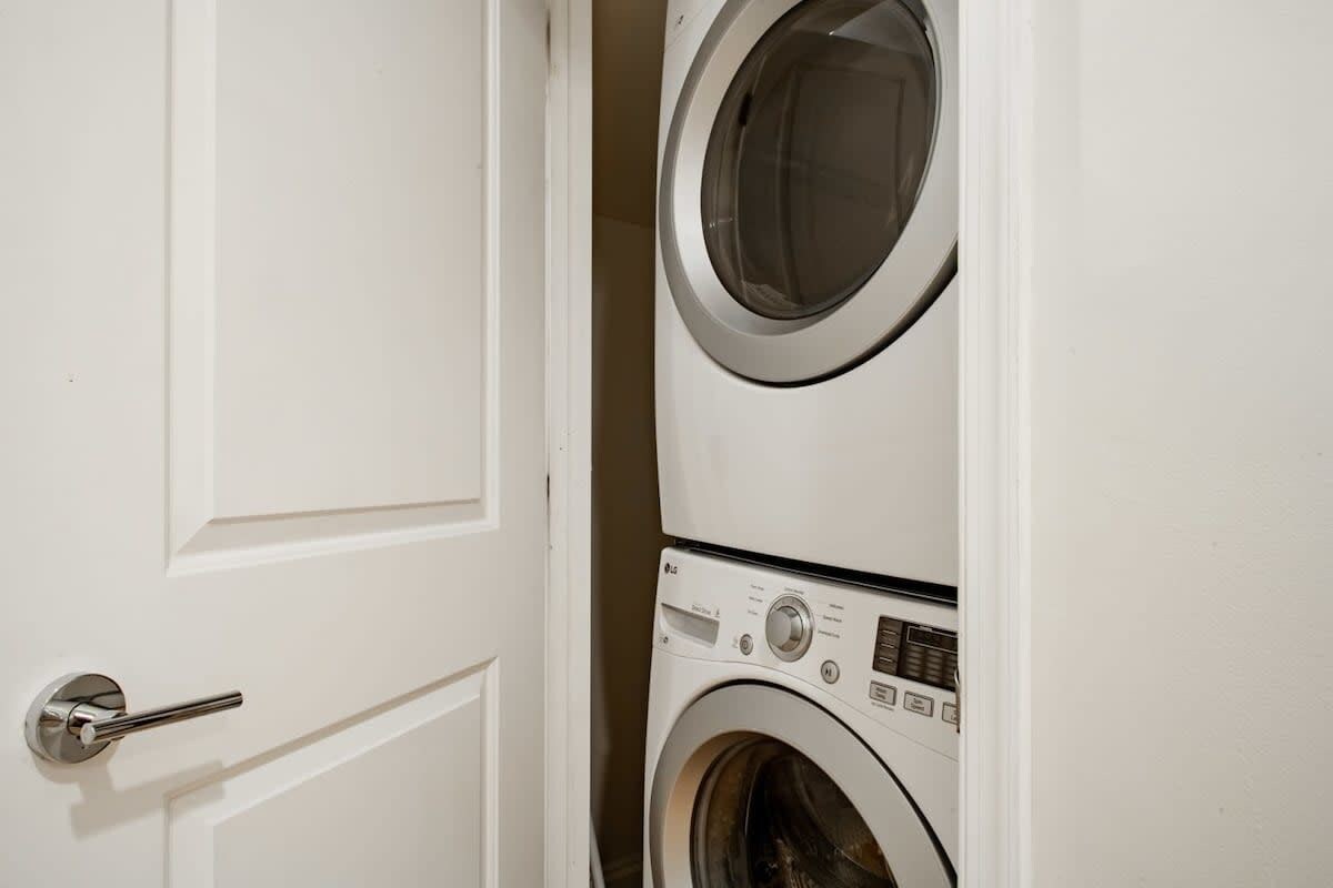 A white door with a silver handle, leading to a laundry room with two stacked washing machines.