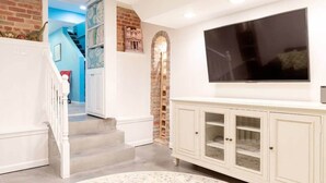 A living room with a white staircase, a TV mounted on the wall, and a white cabinet with glass doors. - FAMILY-FRIENDLY / SUBWAY / ROOFTOP DECK / AU (Washington)