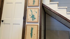 Een trap met een houten leuning en een witte muur met daaraan drie inlijste kaarten van meren.
