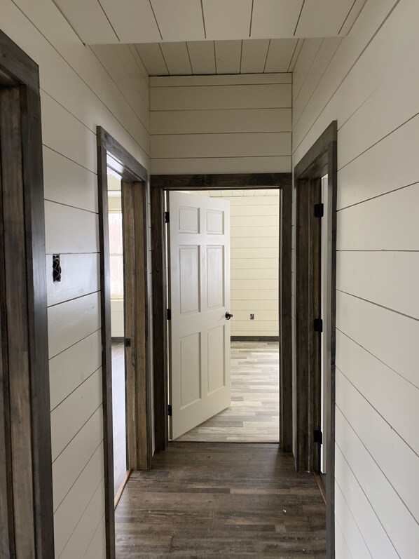 A hallway with white paneled walls and wooden flooring, leading to a door with a white panel design. - Clean and cozy total eclipse retreat, perfect for enjoying the Adirondacks! (Chateaugay)